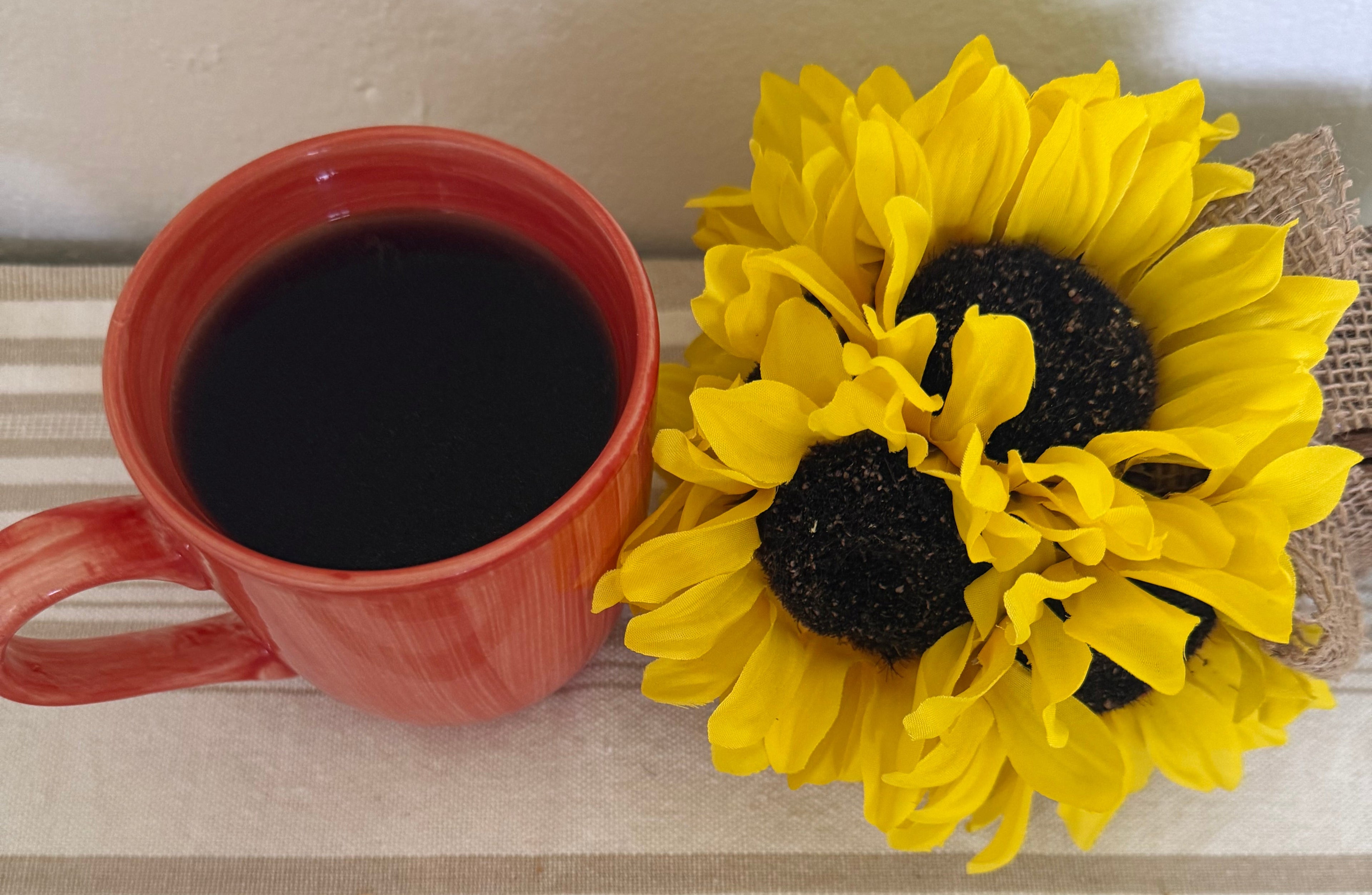 Red mug with black coffee and yellow sunflower decorations on a striped background