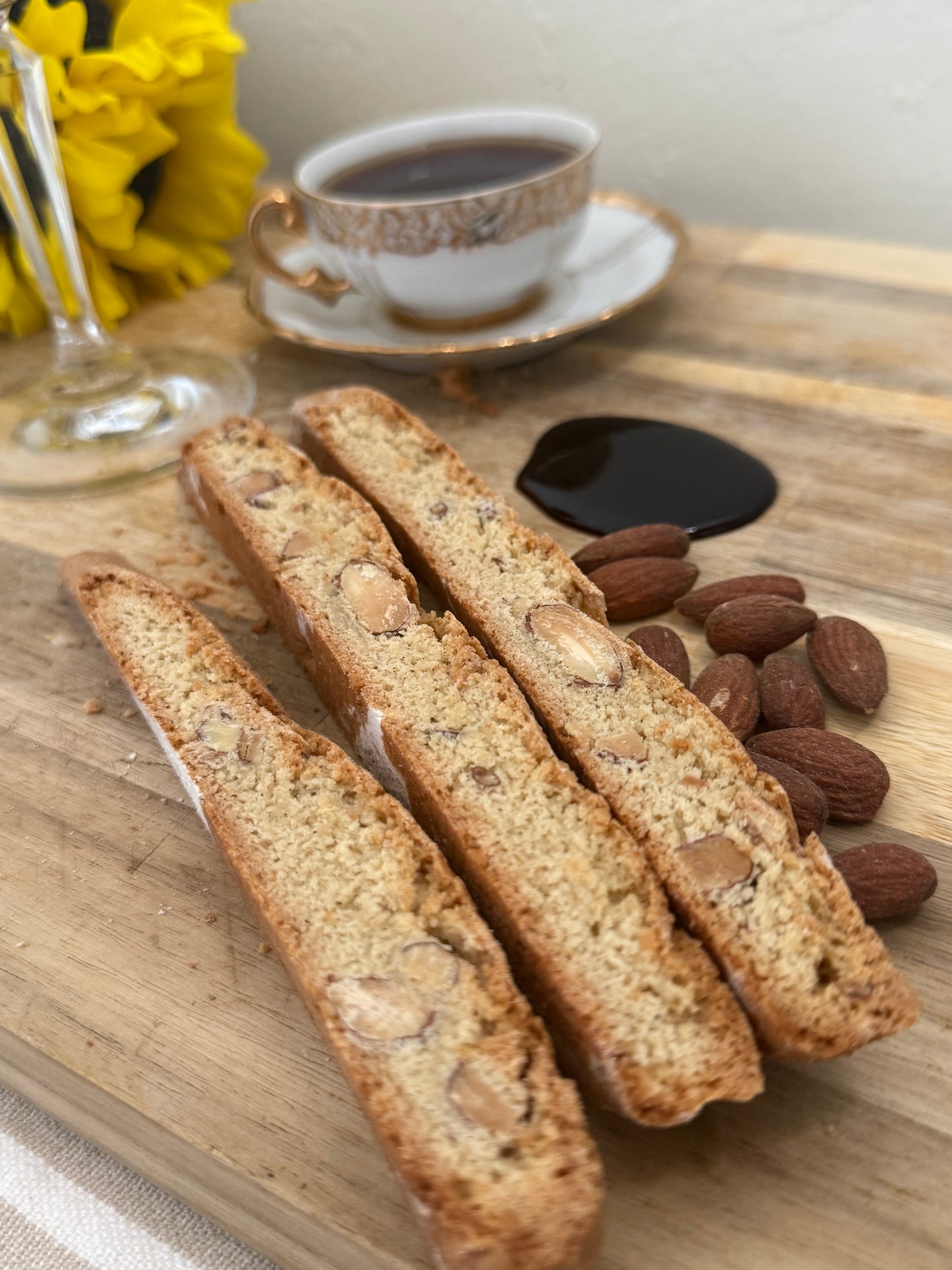 Three biscotti on a wooden board with almonds and a cup of coffee in the background.